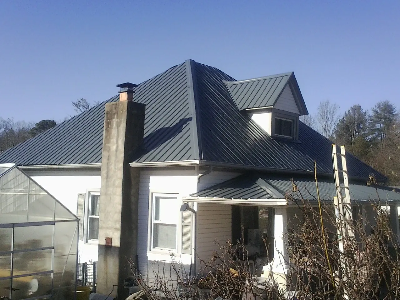 Dark blue standing seam metal roof on a white farmhouse with dormer — Slate & Tile Roof Repair by Roofing Brothers in Coatesville