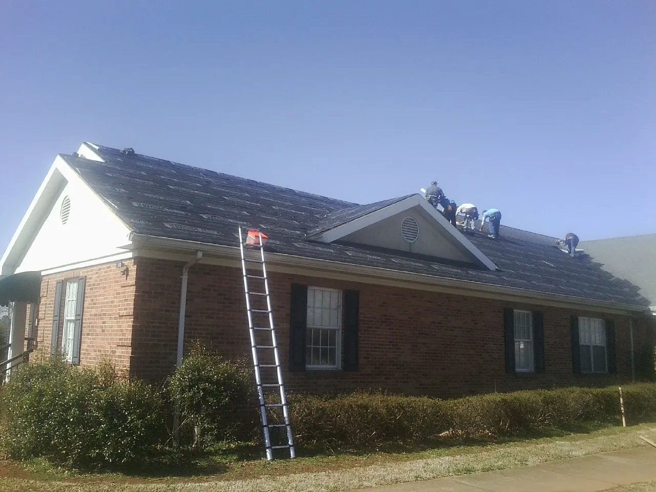 Crew tearing shingles off a brick ranch roof with a ladder set — Metal Roof Repair work by our crew in Coatesville