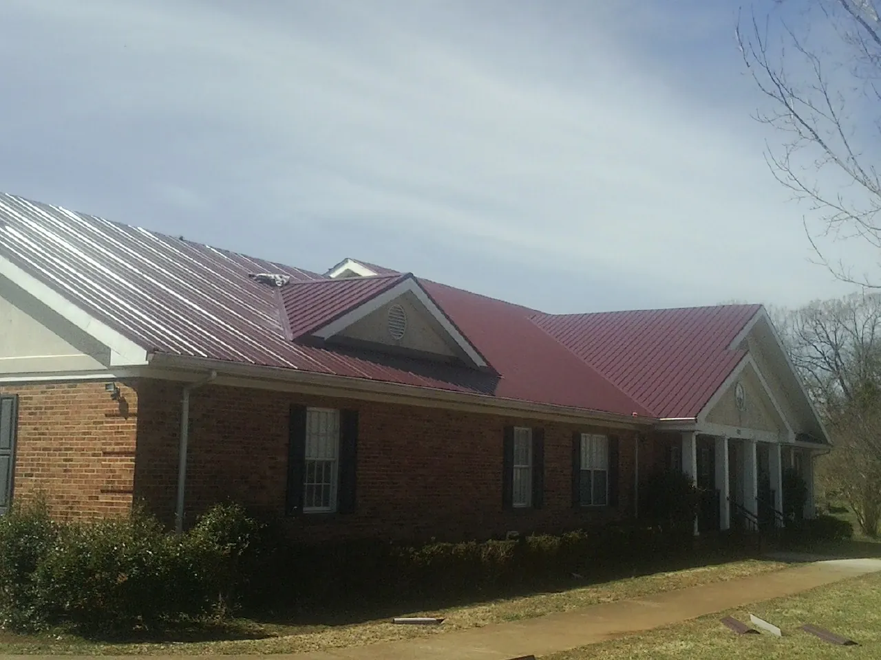 Red metal roof with gabled entries on a long brick building, from a Hail Damage Roof Repair job in Coatesville