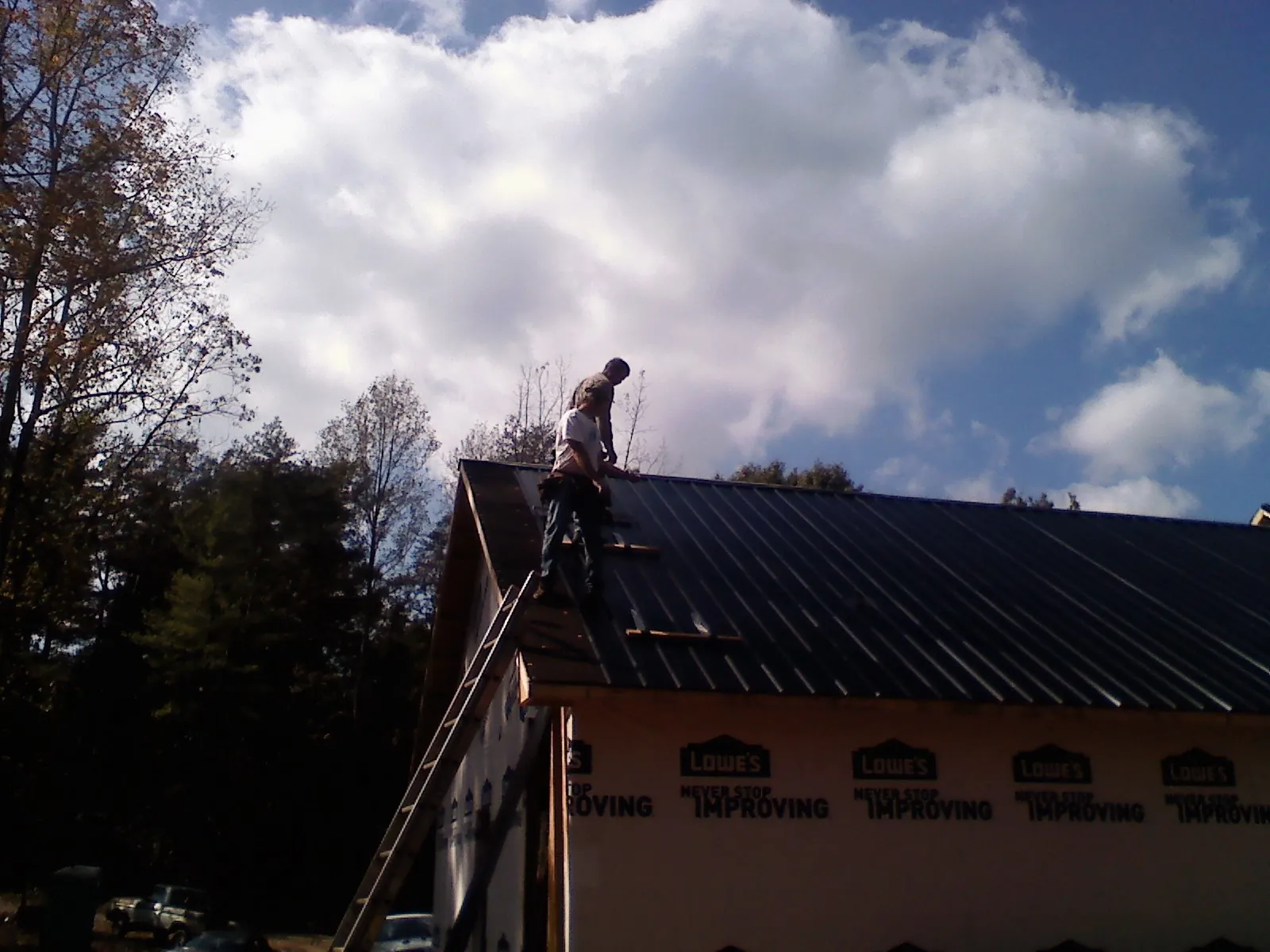 Roofer fastening dark metal panels high against a cloudy sky, from a Roof Inspection job in Coatesville