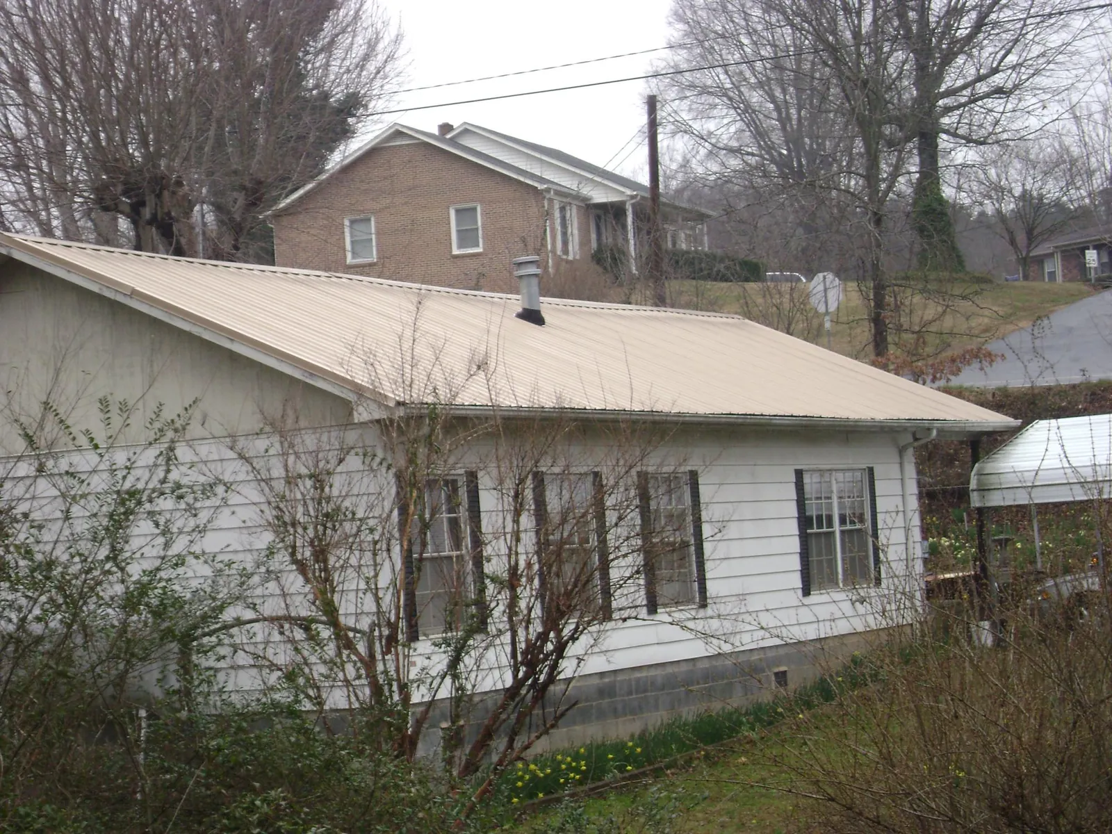 Tan metal roof on a white sided house set into a hillside — Commercial Roofing by Roofing Brothers in Coatesville