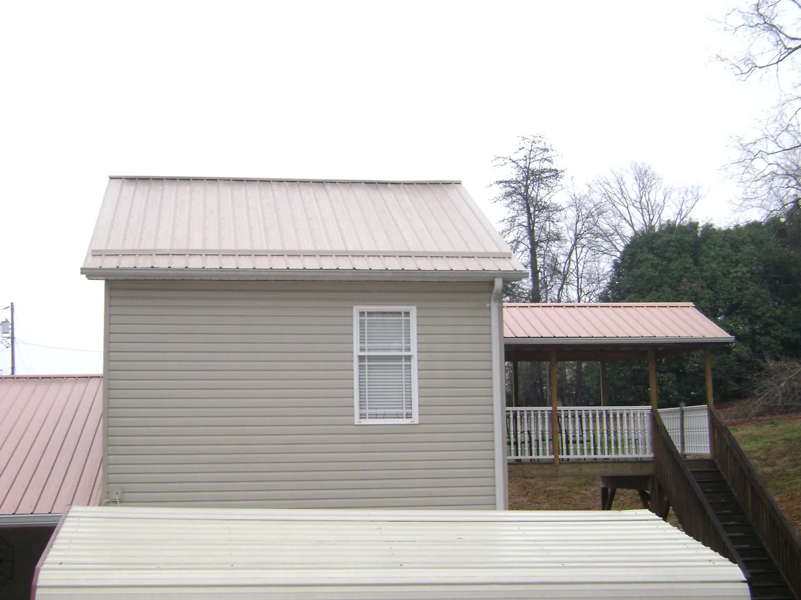 Tan metal roofs on a two story addition and attached porch, from a Roof Replacement job in Coatesville